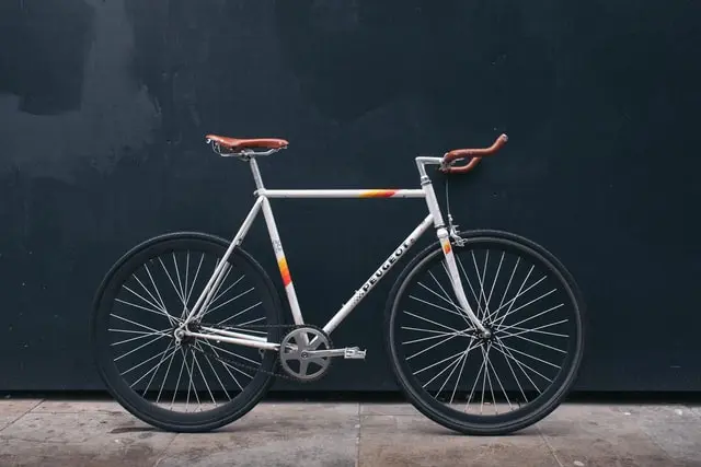Bici a scatto fisso bianca con sella marrone su sfondo scuro