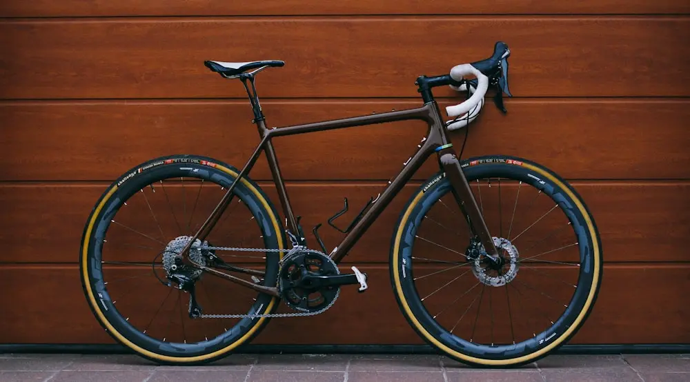 Bici da corsa nera con ruote in carbonio davanti a una parete in legno